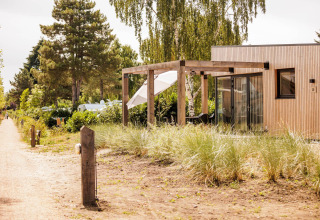 Extérieur du Beachlodge Deluxe au Vakantiepark Leukermeer aux Pays-Bas, terrasse en bois entourée d’arbres.