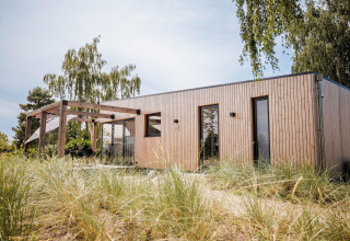 Beachlodge Deluxe moderna en Vakantiepark Leukermeer, Países Bajos, rodeada de naturaleza y árboles verdes.