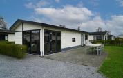 Cabaña Velthorst moderna con grandes ventanales, terraza amplia y mobiliario exterior en día soleado.