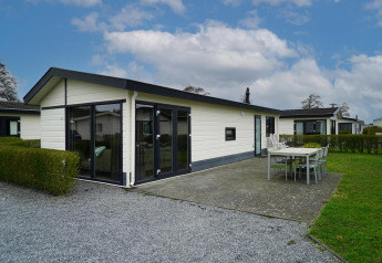 Velthorst-chalet met witte gevel, grote ramen en terras met eettafel en stoelen onder een blauwe lucht.