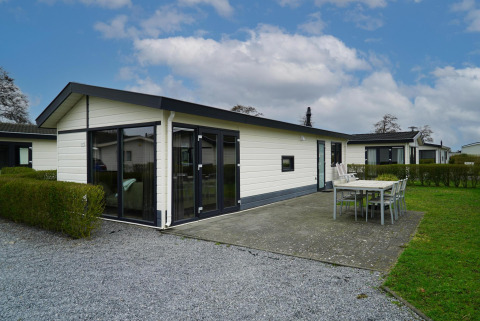 Velthorst-chalet met witte gevel, grote ramen en terras met eettafel en stoelen onder een blauwe lucht.