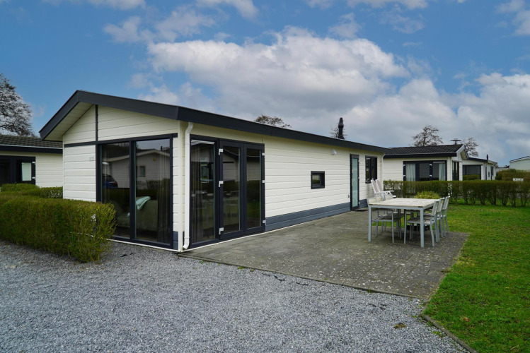 Cabaña Velthorst moderna con grandes ventanales, terraza amplia y mobiliario exterior en día soleado.