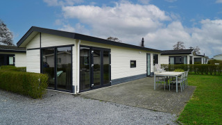 Chalet Velthorst moderne avec grandes baies vitrées, terrasse spacieuse et mobilier d’extérieur, ciel bleu.