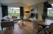 Moderne woonkamer in Velthorst-hut met grijze bank, ronde eettafel, planten en grote ramen met uitzicht.