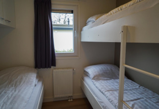 Slaapkamer in de Velthorst cabine met stapelbedden, eenpersoonsbed, raam met gordijn en radiator.