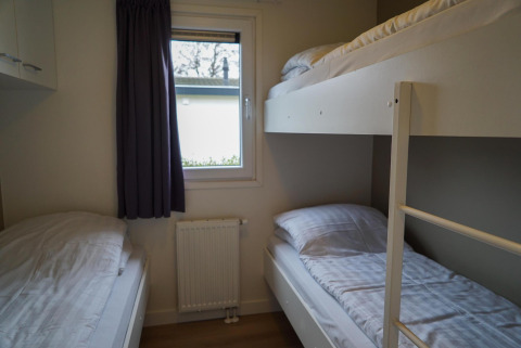 Schlafzimmer in der Velthorst-Hütte mit Etagenbett, Einzelbett, Fenster, Heizung und Vorhang.