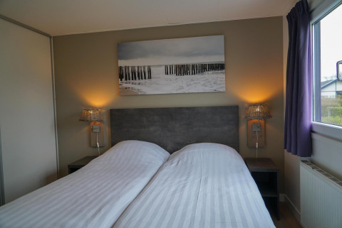 Dormitorio en la cabaña Velthorst con dos camas individuales, lámparas, mesas de noche y cuadro mural.