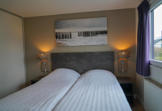 Slaapkamer in de Velthorst cabin met twee eenpersoonsbedden, nachtkastjes, lampen en een wanddecoratie.