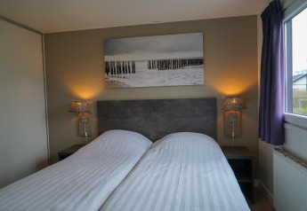 Cozy bedroom at Velthorst cabin with twin beds, bedside tables, lamps, wall art, and a window view.