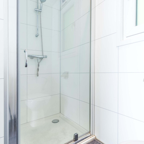 Ducha moderna en un baño con azulejos blancos en la cabaña Velthorst, EuroParcs Parc du Soleil, Países Bajos.