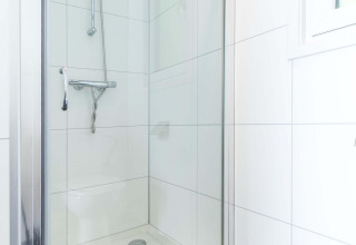 Doccia moderna in un bagno piastrellato bianco presso la cabina Velthorst, EuroParcs Parc du Soleil, Paesi Bassi.