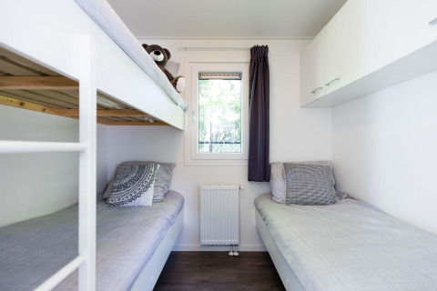 Lichte, moderne slaapkamer met stapelbed en eenpersoonsbed in een Velthorst-hut bij EuroParcs Parc du Soleil.