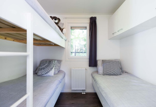 Lichte, moderne slaapkamer met stapelbed en eenpersoonsbed in een Velthorst-hut bij EuroParcs Parc du Soleil.