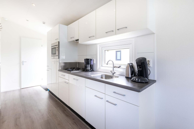 Cocina moderna blanca con electrodomésticos y ventana en cabaña Velthorst de EuroParcs Parc du Soleil, Países Bajos.