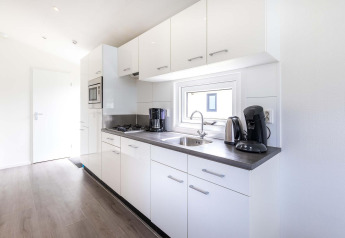 Cocina moderna blanca con electrodomésticos y ventana en cabaña Velthorst de EuroParcs Parc du Soleil, Países Bajos.