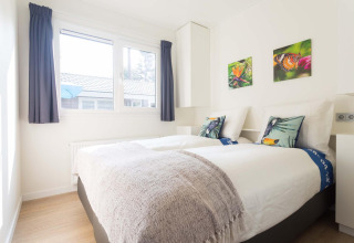 Helles Schlafzimmer in einer Velthorst-Hütte im EuroParcs Parc du Soleil, Niederlande, mit zwei Betten.