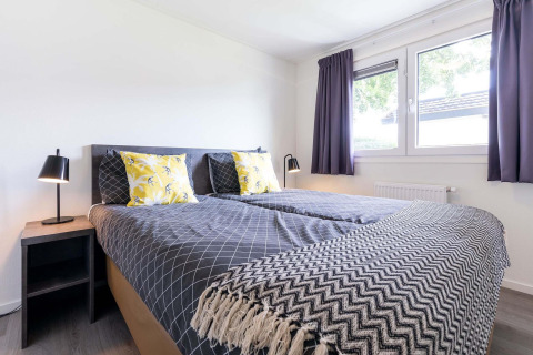 Helles Schlafzimmer mit Doppelbett, modernen Lampen, Fenstern und Vorhängen im Velthorst, Niederlande.
