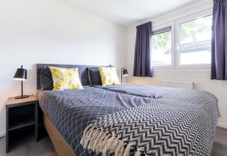 Helles Schlafzimmer mit Doppelbett, modernen Lampen, Fenstern und Vorhängen im Velthorst, Niederlande.