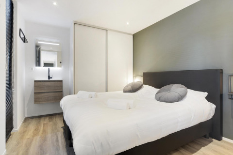 Modern glamping accommodation bedroom featuring a double bed, vanity sink, mirror, and wood flooring.