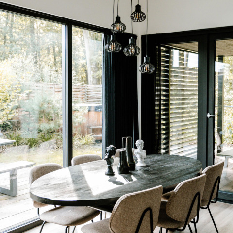 Comedor moderno con mesa ovalada, seis sillas y grandes ventanales visto en un alojamiento glamping.