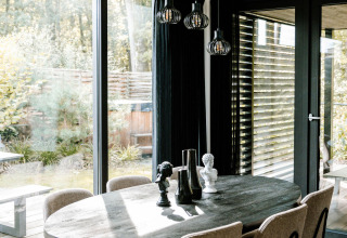 Moderne spiseplads med ovalt bord, seks stole og store vinduer, set på et glampingophold i naturen.