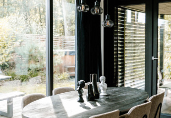 Coin repas moderne avec table ovale, six chaises et grandes baies vitrées dans une location de glamping.