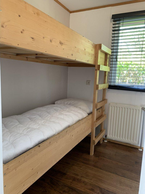 Houten stapelbed met wit dekbed in een kleine kamer van Tiny Chalet, Bungalowpark Het Verscholen Dorp, Nederland.