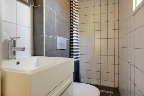 Baño moderno en Tiny Chalet con lavabo blanco, azulejos grises y blancos, y cortina de ducha a rayas.