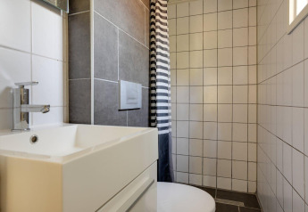 Baño moderno en Tiny Chalet con lavabo blanco, azulejos grises y blancos, y cortina de ducha a rayas.