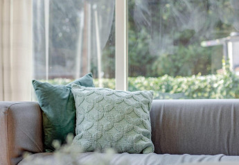 Lichte woonkamer in Tiny Chalet bij Bungalowpark Het Verscholen Dorp in Nederland met groene kussens.