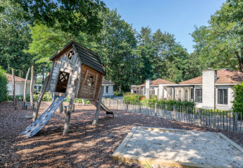 Legeplads og sandkasse foran små chaleter på Bungalowpark Het Verscholen Dorp i Holland omringet af natur.