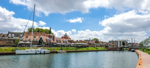Velero atracado junto al canal y casas en Tiny Chalet, Bungalowpark Het Verscholen Dorp, Países Bajos.