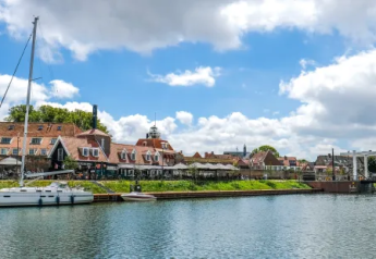 Velero atracado junto al canal y casas en Tiny Chalet, Bungalowpark Het Verscholen Dorp, Países Bajos.