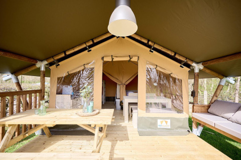 Safari-Zelt Villatent Compact mit Holzveranda, Esstisch, Bank und moderner Einrichtung im Grünen.