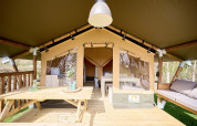 Safari tent Villatent Compact met houten veranda, picknicktafel, bank en moderne inrichting in het groen.