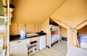 Interno di una tenda safari Villatent Compact con angolo cottura, frigorifero e letti a castello su pavimento in legno.
