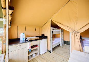 Binnenzicht van een Villatent Compact safaritent met kitchenette, koelkast en stapelbedden op houten vloer.