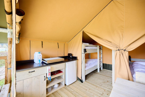 Interno di una tenda safari Villatent Compact con angolo cottura, frigorifero e letti a castello su pavimento in legno.