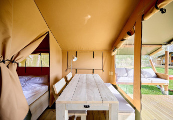 Binnenzicht op een Villatent Compact safaritent met houten tafel, bankjes, bed en buitenzitje.