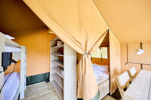 Interieur van een Villatent Compact safaritent met stapelbedden, tweepersoonsbed, rekken en houten tafel.