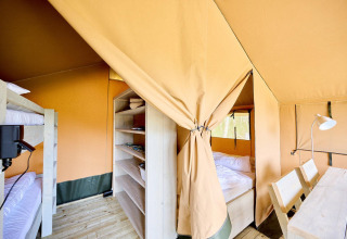 Vista interior de una tienda Villatent Compact con literas, cama doble, estanterías y mesa de madera.
