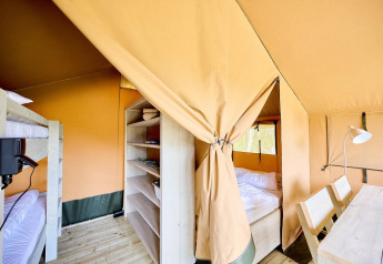 Binnenzicht van een Villatent Compact safaritent met stapelbedden, dubbel bed, rekjes en houten tafel.