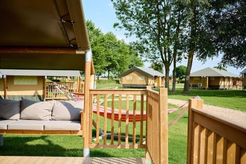 Safari-Zelt mit Terrasse und Hängematte auf Camping Betuwe in den Niederlanden, grün und sonnig.