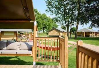 Safari-Zelt mit Terrasse und Hängematte auf Camping Betuwe in den Niederlanden, grün und sonnig.