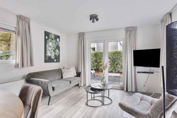 Helles modernes Wohnzimmer mit grauem Sofa, Sesseln, TV und Terrassenzugang in Wellness Lodge, Niederlande.