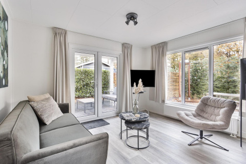 Modern living room at Wellness Lodge, De Thijmse Berg, Netherlands, with sofa, armchair and large windows.
