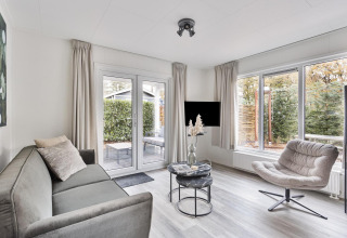 Modern living room at Wellness Lodge, De Thijmse Berg, Netherlands, with sofa, armchair and large windows.