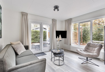 Salón moderno en Wellness Lodge, De Thijmse Berg, Países Bajos, con sofá, sillón y grandes ventanales.