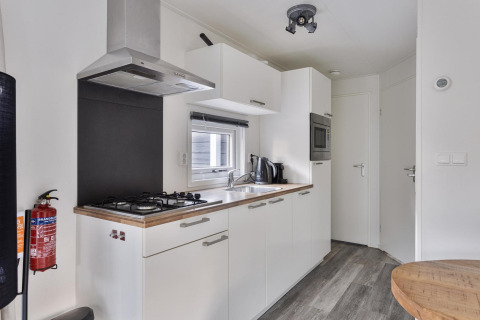 Cocina moderna en lodge con armarios blancos, encimera de gas y fregadero en De Thijmse Berg, Países Bajos.