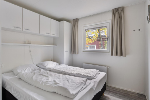 Dormitorio con dos camas individuales, armarios blancos y ventana en Wellness Lodge de De Thijmse Berg, Países Bajos.